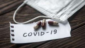 COVID-19 coronavirus concept. Protective mask and pill capsules for treatment of COVID-19. Novel corona virus outbreak, epidemic spread in world. Coronavirus medicine on wooden table.